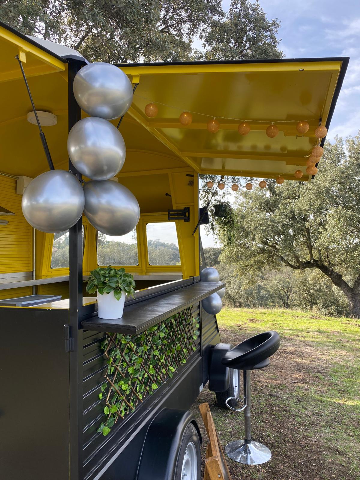 Barra del food truck decorada con globos plateados, plantas y guirnalda de luces